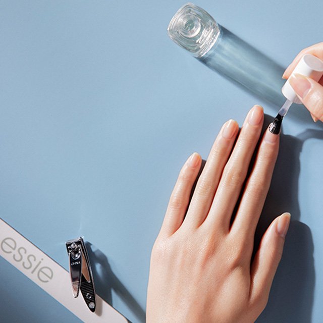 essie Feile, Nagelknipser und Fingernägel auf die ein klarer Unterlack von essie aufgetragen wird.